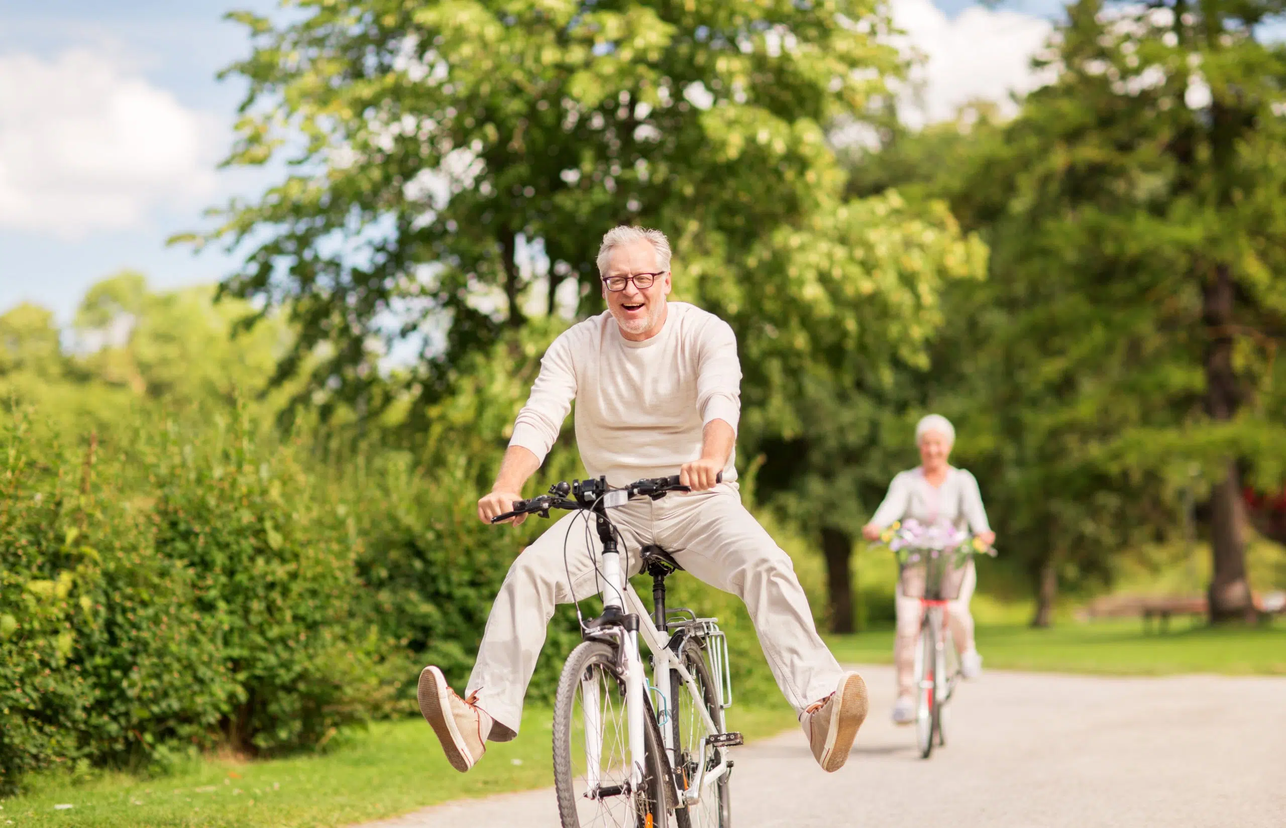 deux personnes seniors faisant du vélo en forêt celui de devant est heureux et a les pieds en l'air car il a des supers aides auditives grâce à phonème