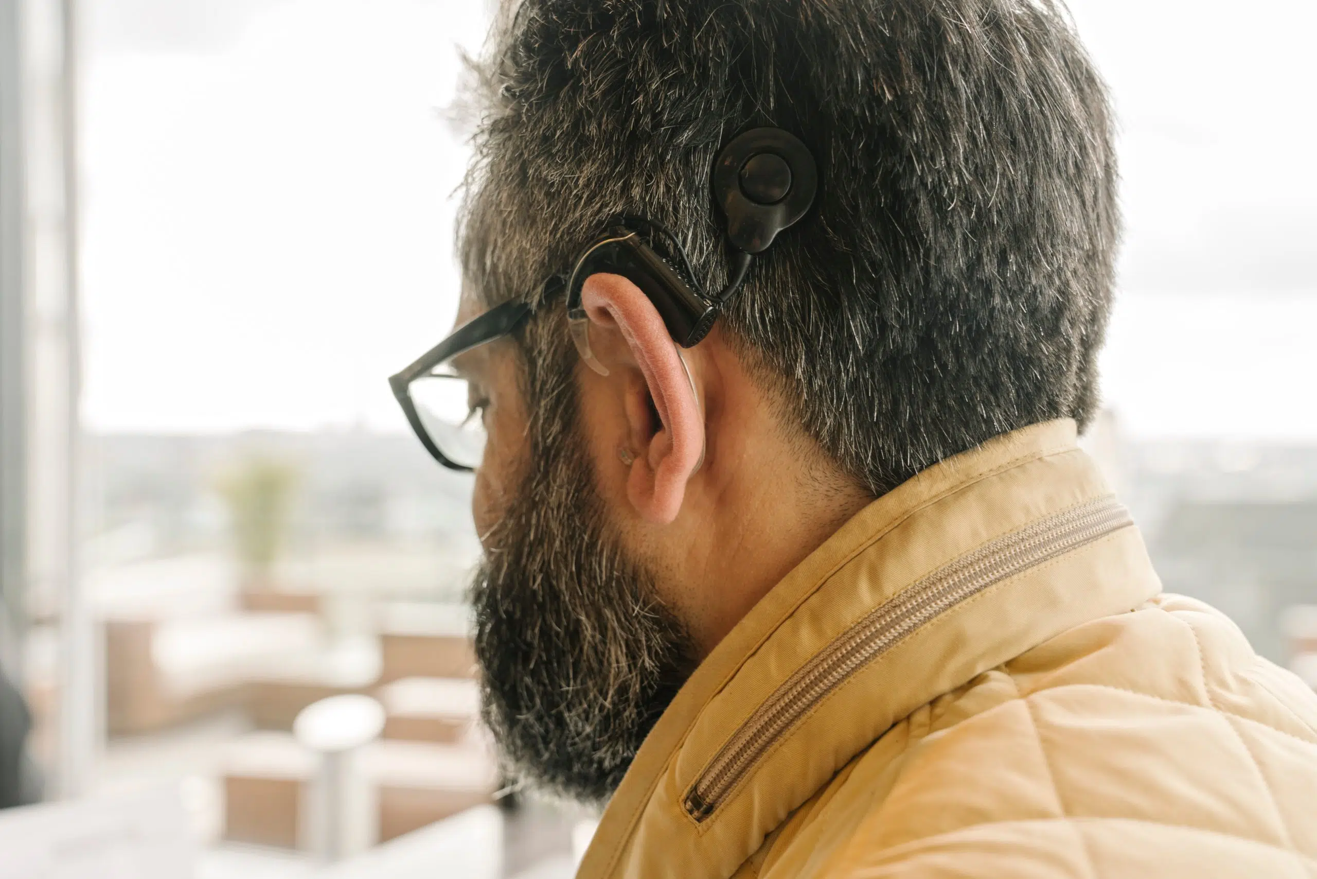 homme barbu quinquagénaire de dos trois quart doté d'un implant cochléaire et suivi par phonème audioprothésiste